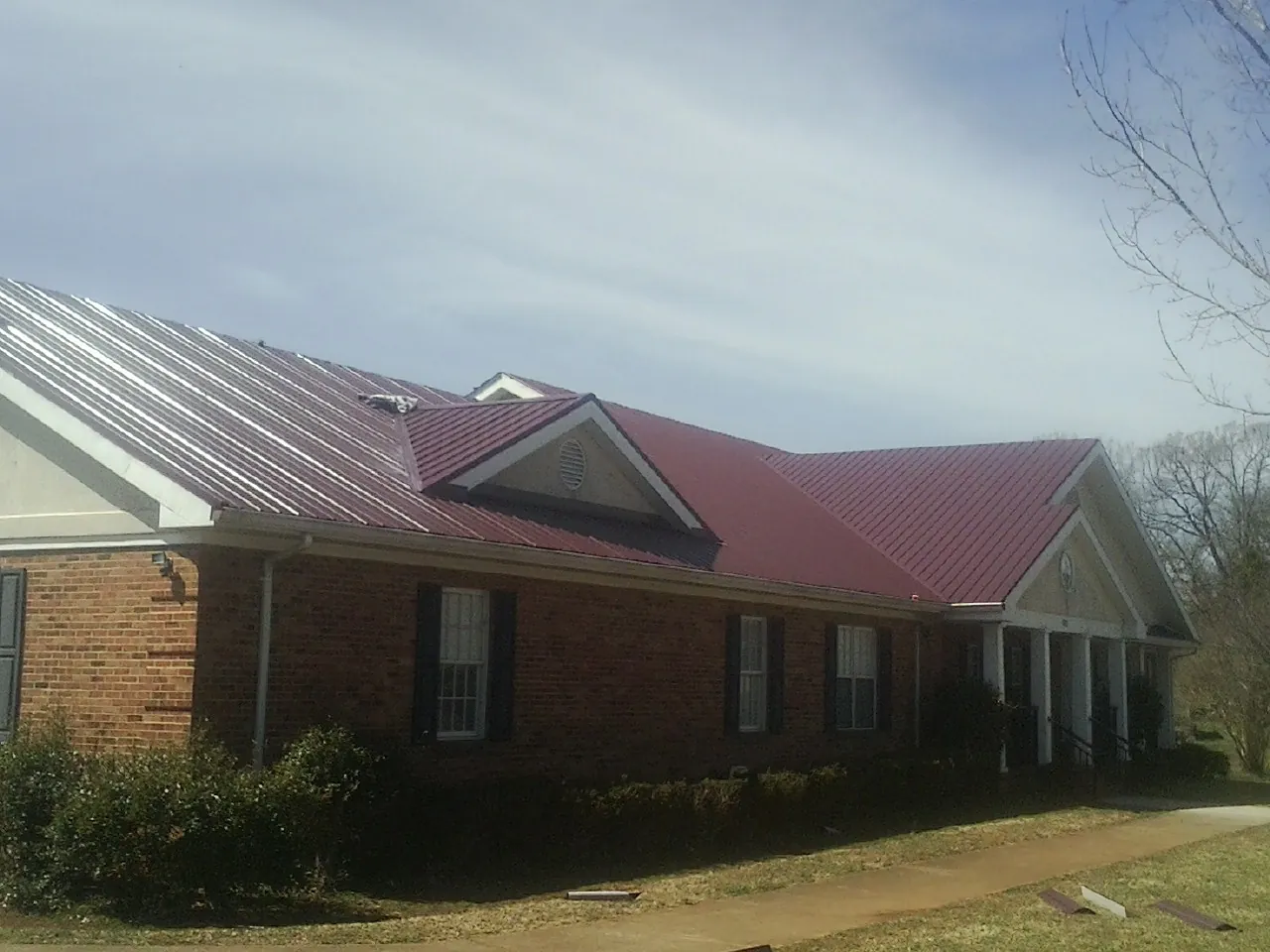Red metal roof with gabled entries on a long brick building, from a Hail Damage Roof Repair job in Goodspring