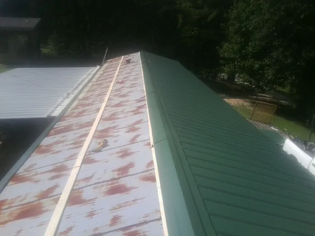 Old rusted panels beside newly installed green metal roofing — Wind Damage Roof Repair by Roofing Brothers in Goodspring