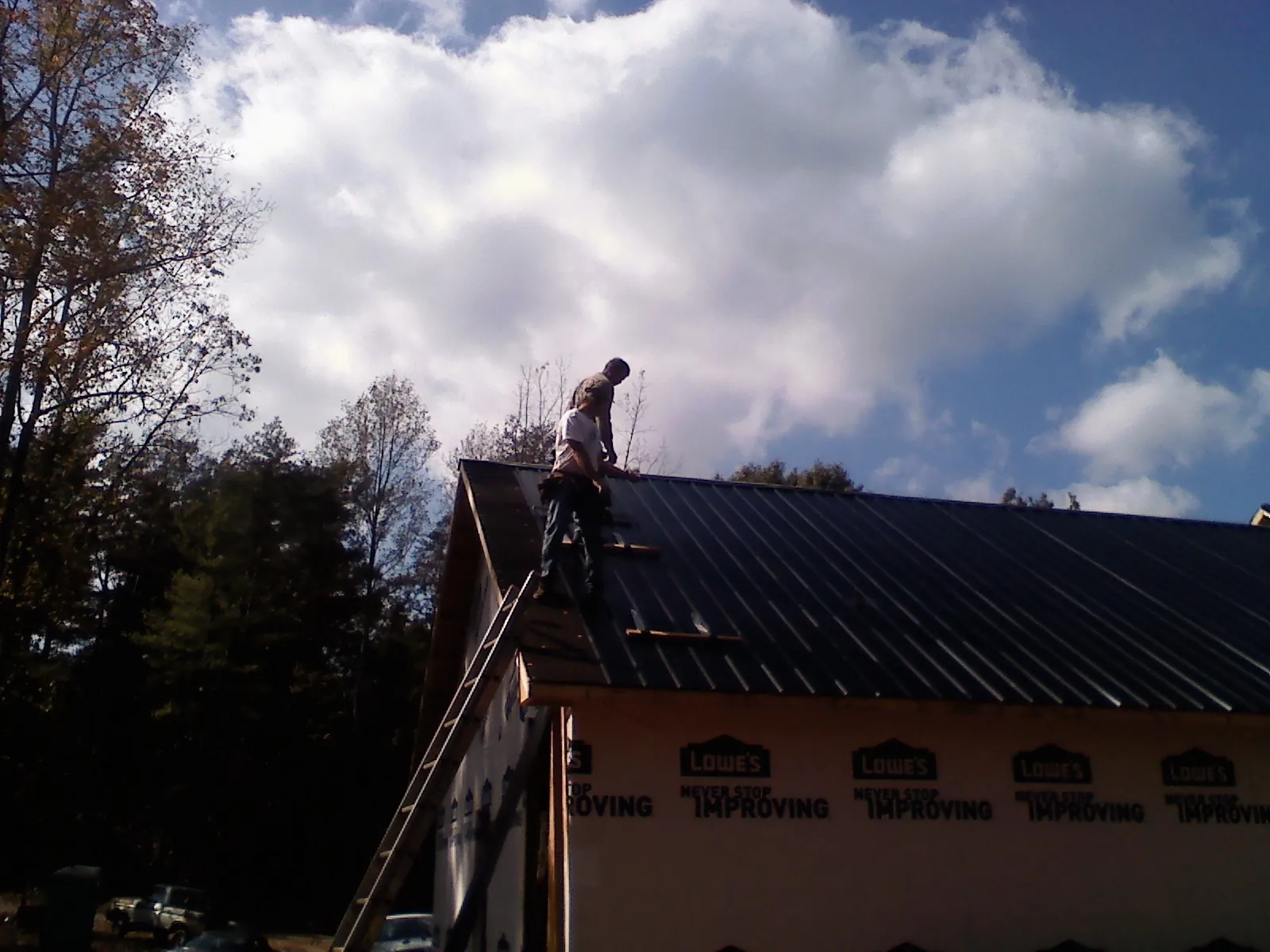 Roofer fastening dark metal panels high against a cloudy sky, from a Roof Inspection job in Goodspring