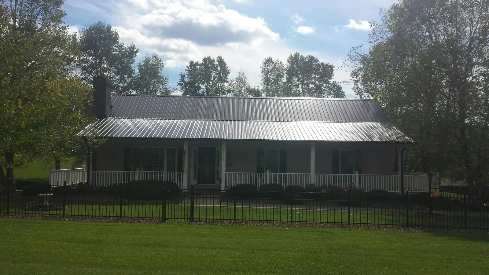 Gray metal roof on a brick ranch with a full width front porch — Gutter Guard Installation work by our crew in Goodspring